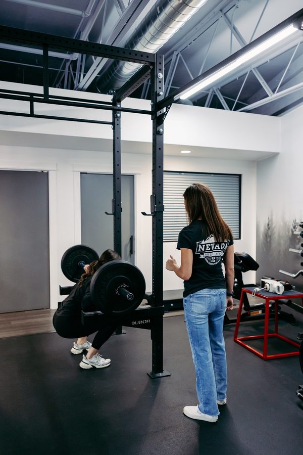 A clinician watching a woman perform a loaded barbell squat